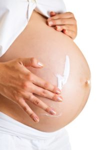 Pregnant woman moisturising belly to avoid stretch marks isolated on white